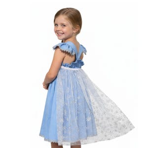 May include: A light blue dress with a white snowflake-patterned overlay. The dress features ruffled cap sleeves and a white waist band. The skirt is a flared style, and the dress is designed for a child.