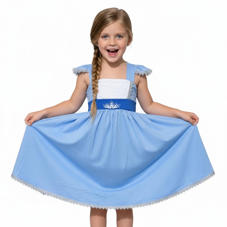 May include: A light blue dress with a white bodice and a blue belt featuring a silver snowflake design. The dress has short sleeves with lace trim and a matching lace trim at the hem. The girl is smiling and holding the dress out.