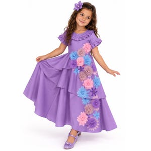 May include: A floor-length purple dress with ruffled sleeves and a cascading diagonal arrangement of fabric flowers in shades of pink, blue, and lavender. The dress features a matching purple hair accessory with a flower design and purple shoes.