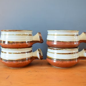 May include: Four brown and white striped ceramic soup bowls with handles. The bowls are stacked in pairs.
