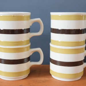 May include: Four stacked mugs with brown and yellow stripes. The mugs are made of ceramic and have a white background.