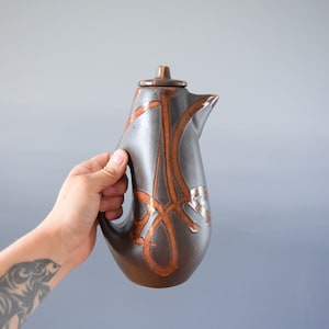 May include: A brown ceramic jug with a lid and a handle. The jug has a unique design with brown and orange lines.