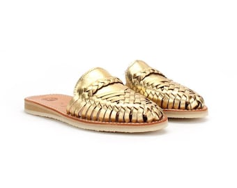 Puede incluir: Un par de sandalias de cuero doradas con un diseño tejido. Las sandalias tienen una suela plana y una punta puntiaguda.