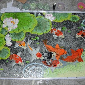 May include: A mosaic art piece depicting a pond scene with colorful koi fish swimming among lily pads and water ripples. The mosaic is made of small, colorful glass tiles.