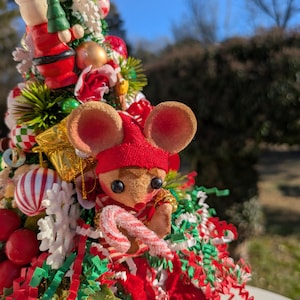 May include: A miniature Christmas tree decorated with red and green tinsel, ornaments, and a small mouse figurine holding a candy cane.