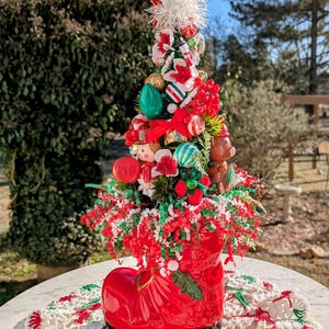 May include: A miniature Christmas tree decorated with ornaments, candy canes, and a small toy soldier, all nestled in a red boot planter. The boot sits on a white crocheted doily.