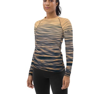 Op de afbeelding: Een shirt met lange mouwen met een waterrimpelpatroon in beige en blauwe tinten. Het shirt heeft een ronde hals en de tekst "La Mer" is gedrukt op de rechtermouw.