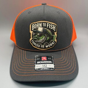 以下が含まれることがあります： 黒とオレンジのトラッカーハット。パッチには「Born to Fish, Forced to Work!」の文字と、サングラスをかけたアニメーションの魚が描かれています。帽子は調節可能で、リチャードソンのロゴが付いています。