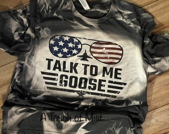 May include: Grey t-shirt with a bleached design. The shirt features aviator sunglasses with the American flag design and the text "TALK TO ME GOOSE". A jet plane graphic is centered between the lenses.