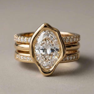 Könnte beinhalten: Ein Set aus drei goldenen Ringen. Der oberste Ring hat einen großen, oval geformten, klaren Edelstein in einer einzigartigen, unregelmäßigen Lünette. Der mittlere Ring ist ein schlichtes Goldband, und der untere Ring ist ein Goldband mit kleinen, klaren Edelsteinen.