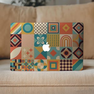 May include: A laptop skin featuring a grid of colorful geometric patterns including circles, squares, diamonds, dots, and arches in shades of teal, orange, yellow, and dark brown, with a white Apple logo centered on the rectangular surface.
