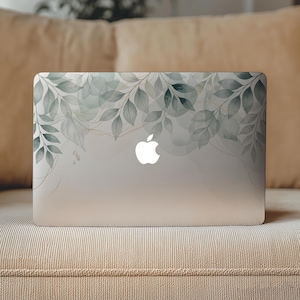 Op de afbeelding: Een zilveren laptop met een decoratieve skin met een botanisch aquarelpatroon van saliegroene en donkergroene bladeren. Het ontwerp bevat subtiele gouden lijntekeningen en het witte Apple-logo in het midden van het metalen oppervlak.