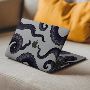 Op de afbeelding: Een grijze laptop met een ontwerp van donkerpaarse octopus tentakels. De tentakels, met gedetailleerde zuignappen, zijn over het oppervlak van de laptop geplaatst. Het Apple-logo is zichtbaar.