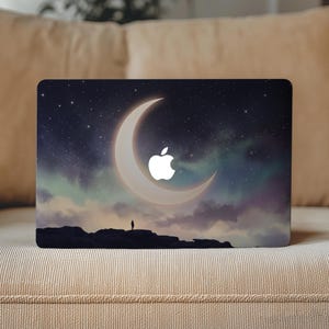 May include: A laptop skin featuring a night sky illustration with a large crescent moon, a starry background, and a silhouette of a person standing on a rocky cliff. The white Apple logo is centered within the crescent moon shape on the laptop lid.