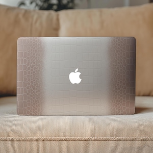 May include: A laptop with a textured, embossed crocodile skin pattern in a gradient of beige and brown tones. The surface features a repeating scale-like design that transitions from darker edges to a lighter centre, with a white Apple logo centred.