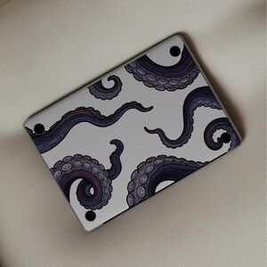Op de afbeelding: Een witte laptophoes met een herhaald patroon van donkerpaarse octopus tentakels. De tentakels zijn gedetailleerd met cirkelvormige zuignappen. De hoes heeft zwarte voetjes.