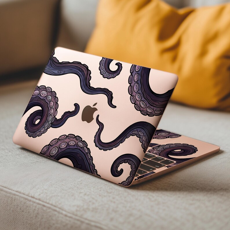 Op de afbeelding: Een ros&eacute;gouden laptop met een ontwerp van donkerpaarse octopus tentakels. De tentakels hebben een gedetailleerd, gestructureerd uiterlijk met zuignappen. Het Apple-logo is zichtbaar. De laptop is open en toont het toetsenbord en het scherm.