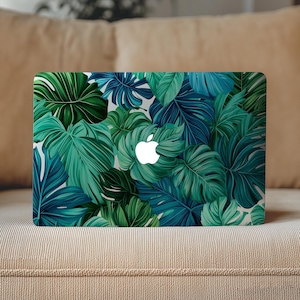 Op de afbeelding: Laptophoes met een tropisch bladerpatroon in groen- en blauwtinten. De hoes heeft een wit Apple-logo in het midden. De bladeren zijn gelaagd, waardoor een textuur ontstaat. De laptop ligt op een beige bank.