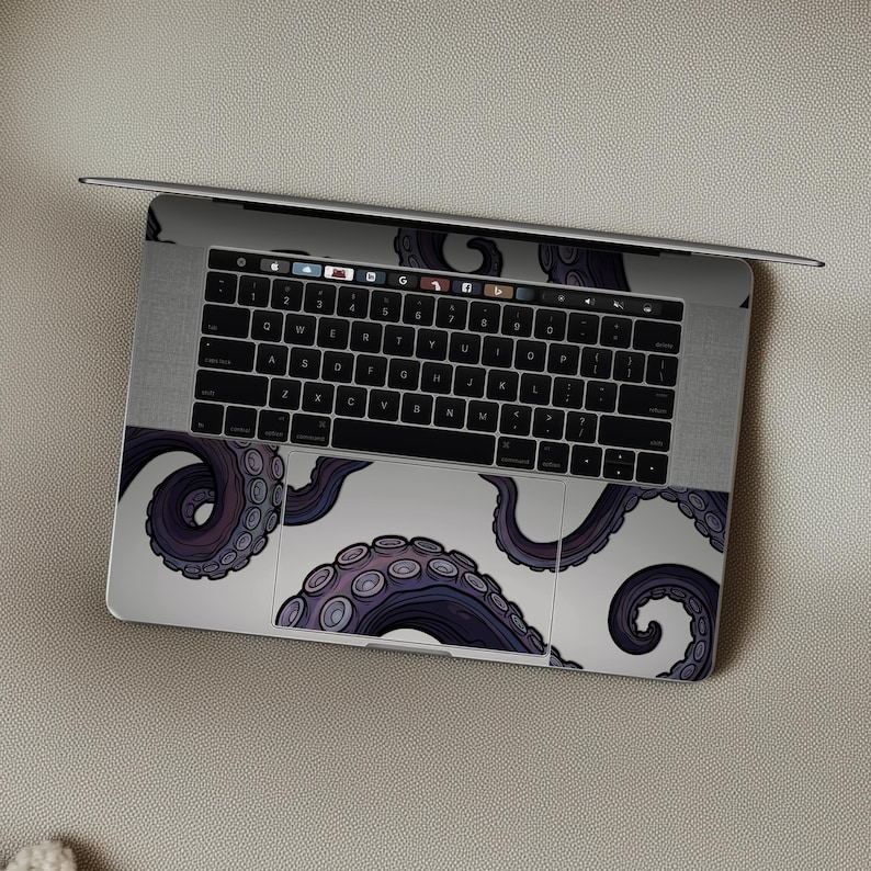 Op de afbeelding: Een laptop met een wit en paars octopus tentakel ontwerp op het toetsenbord en touchpad. De tentakels zijn diep paars met lichtere paarse zuignappen, tegen een witte achtergrond. De laptop is open op een neutrale ondergrond.