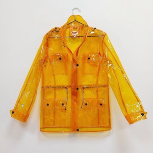 May include: A transparent yellow raincoat with a collared neckline, four front pockets, and black button closures. The jacket is hanging on a silver hanger against a white background. The raincoat has long sleeves and a drawstring at the waist.