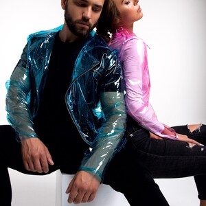 May include: A couple wearing clear plastic jackets. The man is wearing a blue jacket and the woman is wearing a pink jacket. They are both sitting on a white cube.