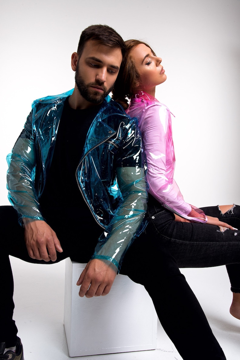 May include: A couple wearing clear plastic jackets. The man is wearing a blue jacket and the woman is wearing a pink jacket. They are both sitting on a white cube.