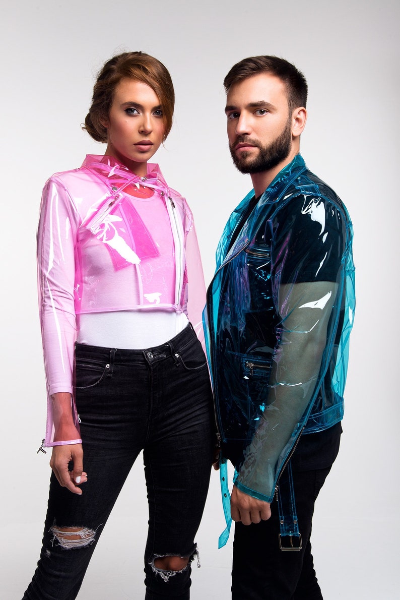May include: Two people wearing clear plastic jackets, one pink and one blue. The person on the left is wearing black jeans with distressed knees. The person on the right is wearing black jeans with a black belt.