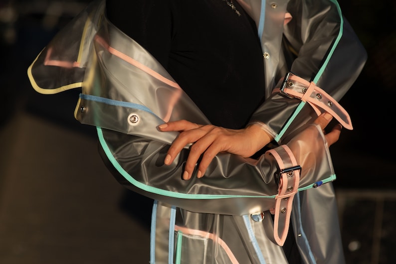 May include: A clear plastic raincoat with colorful trim. The raincoat has a light blue, pink, and yellow trim. The raincoat has a belt and a snap closure.