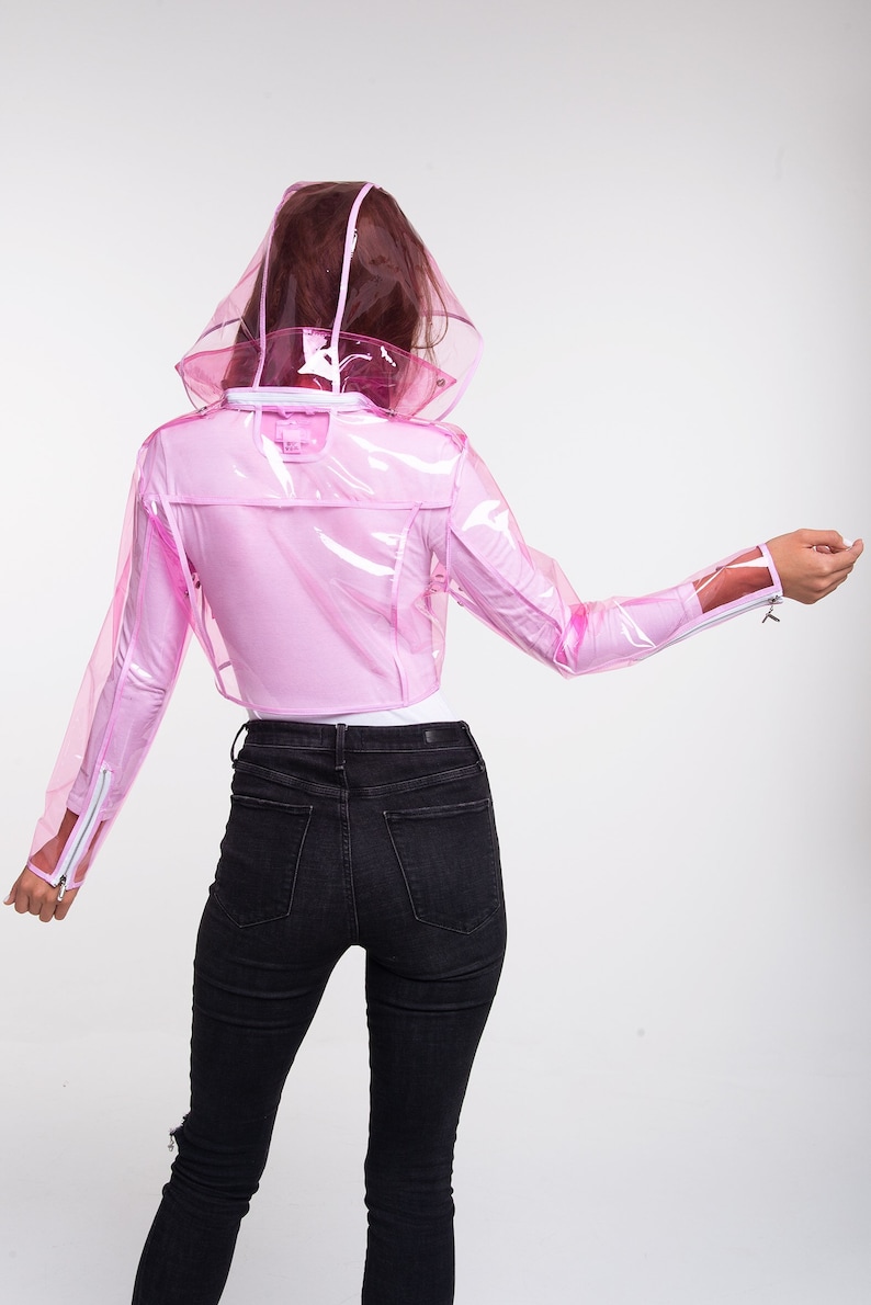 May include: A pink transparent raincoat with a hood. The raincoat is cropped and has a zipper closure. The model is wearing black jeans.