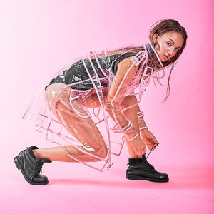 May include: A woman wearing a transparent pink raincoat with white trim, black clothing, and black lace-up boots. She is tying the laces of her boots while standing on a pink background.