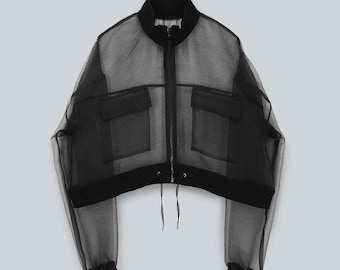 May include: Black sheer bomber jacket with a zip-up front, two front pockets, and a drawstring hem. The jacket has long sleeves with ribbed cuffs and a stand-up collar. The fabric is lightweight and appears to be semi-transparent.