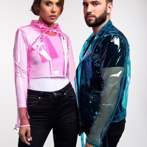May include: Two people wearing clear plastic jackets, one pink and one blue. The person on the left is wearing black jeans with distressed knees. The person on the right is wearing black jeans with a black belt.