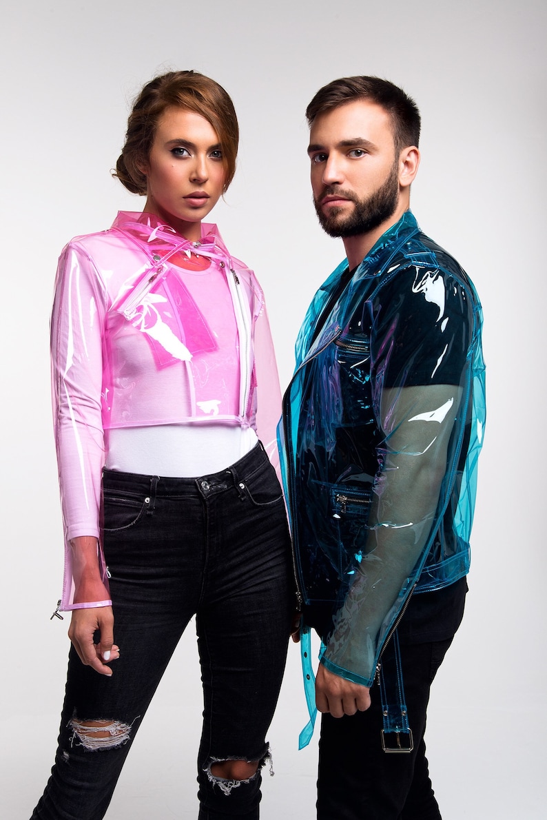 May include: Two people wearing clear plastic jackets, one pink and one blue. The person on the left is wearing black jeans with distressed knees. The person on the right is wearing black jeans with a black belt.