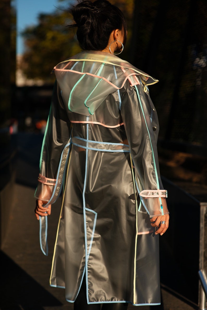 May include: A transparent raincoat with colorful trim. The raincoat has a hood and a belt. The raincoat is made of a clear plastic material and has a light blue, pink, and yellow trim.