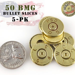 May include: Five gold-colored 50 BMG bullet slices, each with a different marking, including "PSD" and "C", on a white surface. The bullet slices are about the size of a US quarter.
