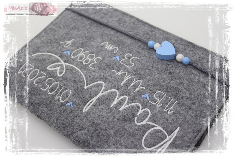 May include: Grey felt pouch with white embroidery that reads "Still my boy" and "06.08.2023" with a blue heart and white beads attached to a string.