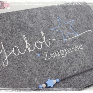 Könnte beinhalten: Graue Filztasche mit einem weißen gestickten Stern und dem Text "Jakob Zeugnisse".