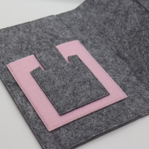 Pu&ograve; includere: Una pochette in feltro grigio con una tasca in feltro rosa all'interno. La pochette &egrave; aperta e la tasca &egrave; visibile.