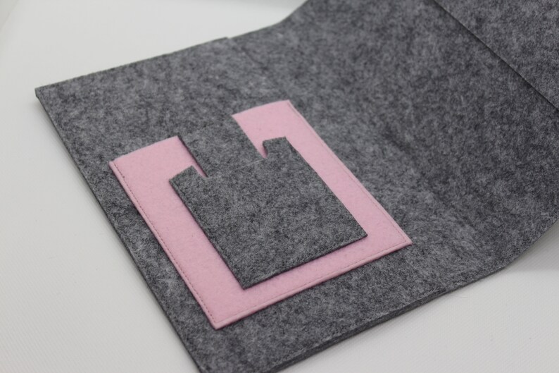 Pu&ograve; includere: Una pochette in feltro grigio con una tasca in feltro rosa all'interno. La pochette &egrave; aperta e la tasca &egrave; visibile.