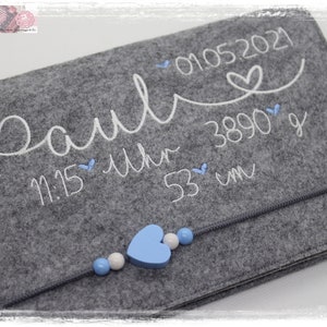 May include: Grey felt baby keepsake with white embroidery that reads "Paul 01.05.2021 11:15 Uhr 3890 g 53 cm" with a blue heart and beads.