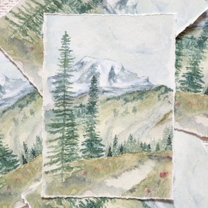 以下が含まれることがあります： 前景に常緑樹がある山岳風景の水彩画。このアートワークは、曇り空の下の雪をかぶった山を特徴としています。絵画は、テクスチャ加工された、破れたエッジを持っています。