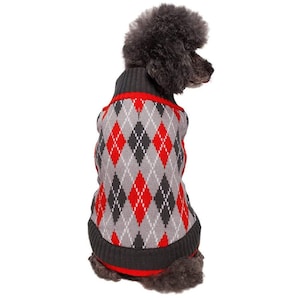Puede incluir: Un suéter para perros con un patrón de rombos gris, rojo y negro. El suéter tiene un cuello alto y un ribete rojo. El perro es de una raza pequeña y de color oscuro.