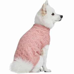 May include: A light pink cable-knit dog sweater. The sweater has a turtleneck and covers the dog's torso. The dog is white with a fluffy tail and is sitting on a white background.