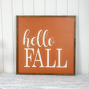 May include: A wooden framed sign with an orange background and white lettering that says "hello fall".