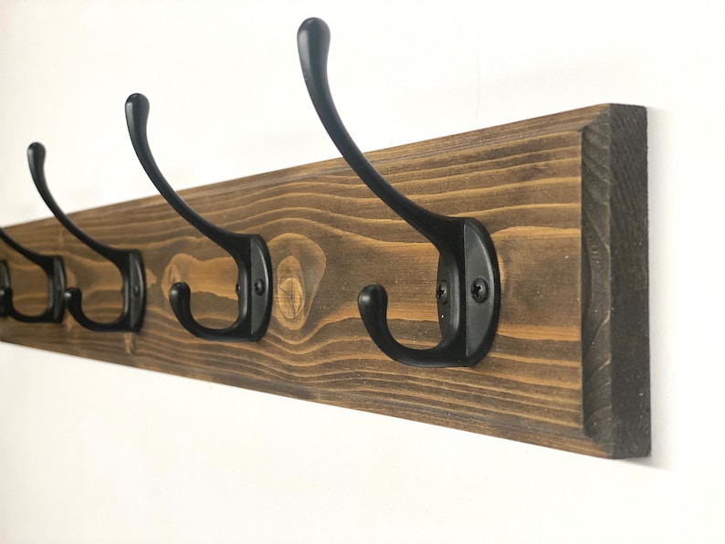 May include: A wooden coat rack with five black metal hooks. The rack is stained a dark brown color and has a rustic look.