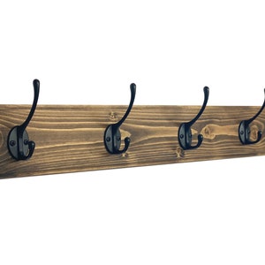 May include: A rustic wooden coat rack with five black metal hooks. The rack is stained a dark brown color and has a natural wood grain.