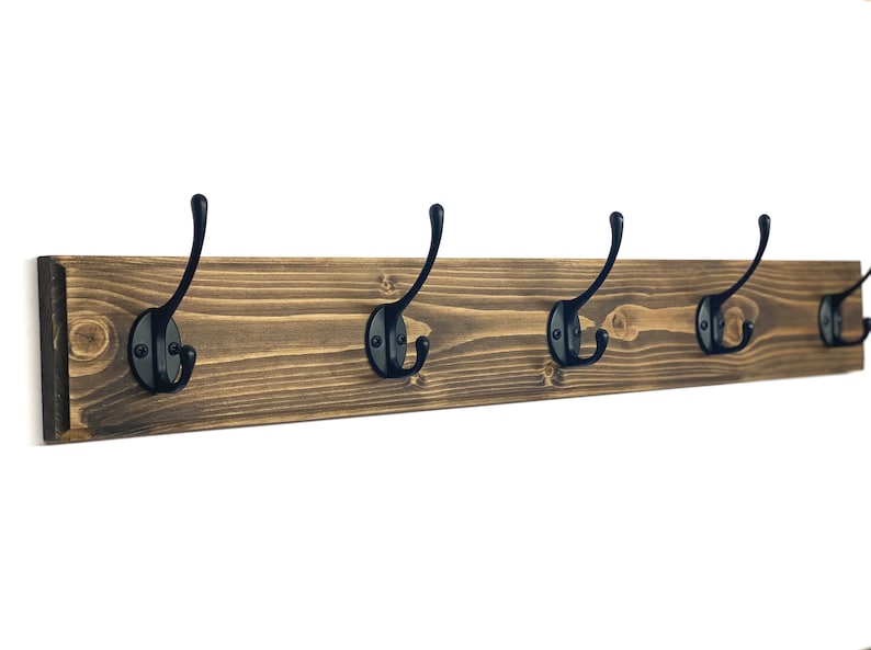 May include: A rustic wooden coat rack with five black metal hooks. The rack is stained a dark brown color and has a natural wood grain.