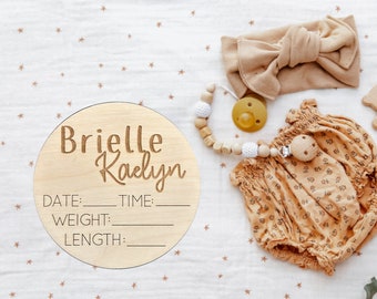 May include: A wooden baby announcement plaque with the names Brielle Kaelyn and spaces to fill in the date, time, weight, and length. The plaque is on a white background with brown stars.