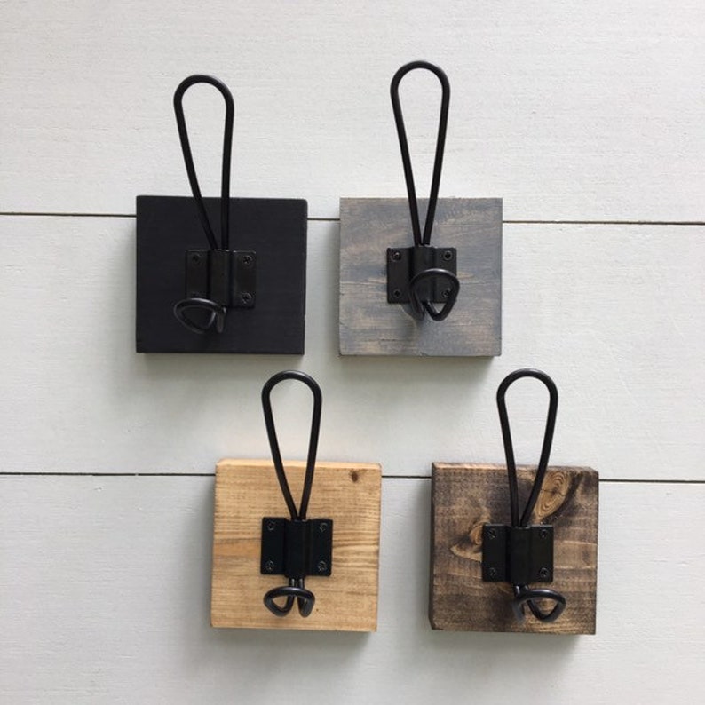 K&ouml;nnte beinhalten: Vier Wandhaken aus Holz mit schwarzen Metallhaken. Die Haken sind in vier verschiedenen Holzbeizen: Schwarz, Grau, Naturholz und Dunkelbraun.