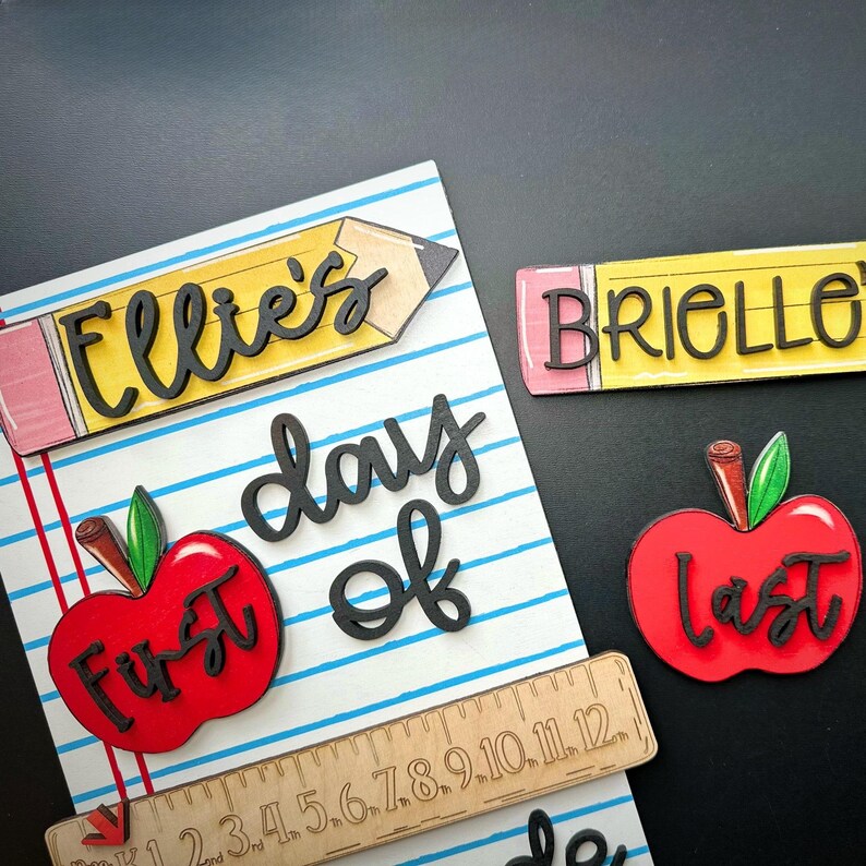 May include: A collection of back-to-school themed wooden cutouts. Includes a pencil with "Ellie's" and "Brielle" on them, a red apple with "First" and "Last", a ruler, and the words "day of".